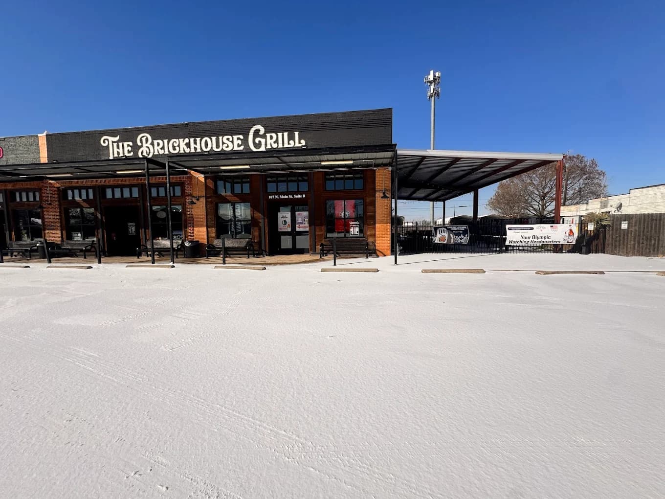 The Brickhouse Grill restaurant front and snow-covered parking lot under a clear blue sky.