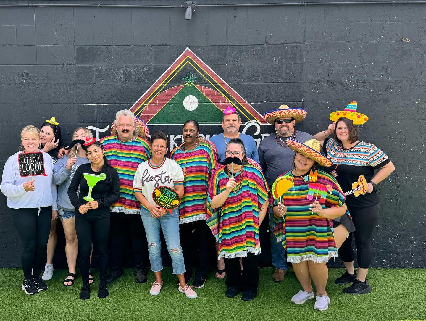 Group of people in vibrant ponchos and sombreros posing with festive fiesta-themed party props.