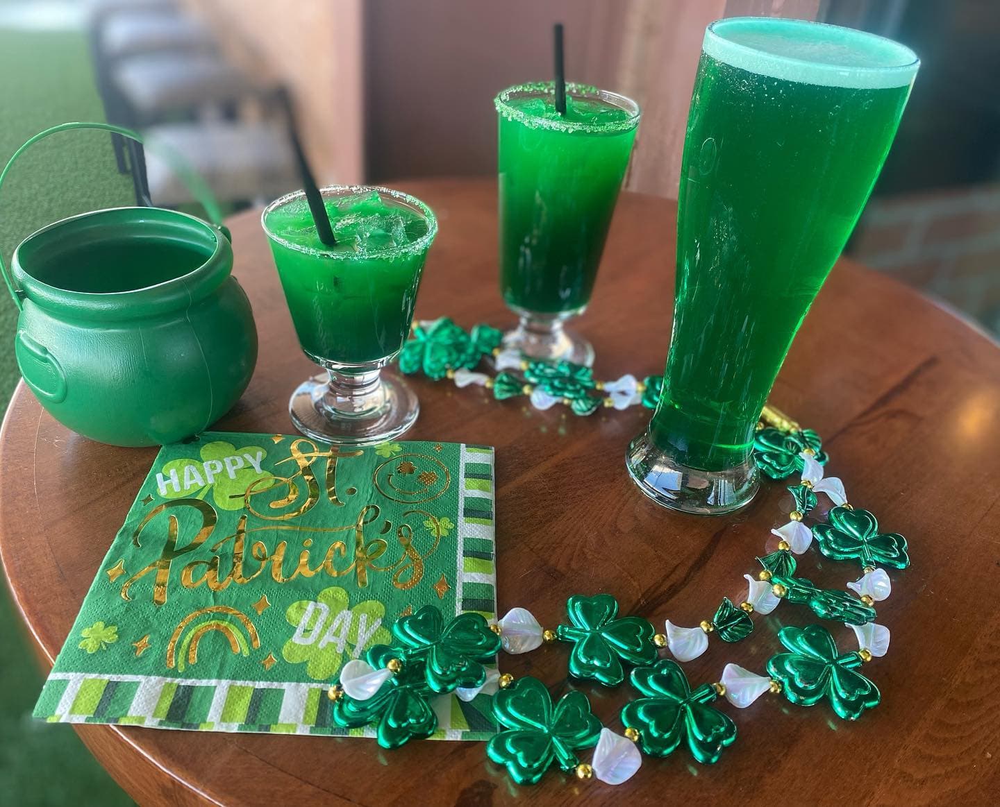 Three green drinks, shamrock beads, a green cauldron, and a St. Patrick's Day napkin.