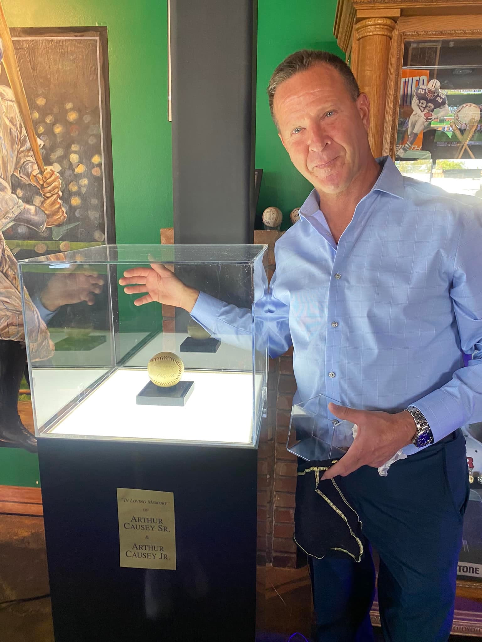 Man stands next to a memorial display case featuring a baseball for Arthur Causey.