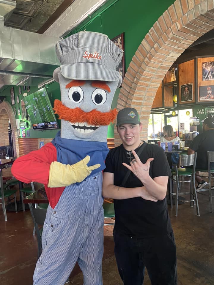 Young man posing with Spike, a railroad mascot wearing a conductor's hat and pinstriped overalls.