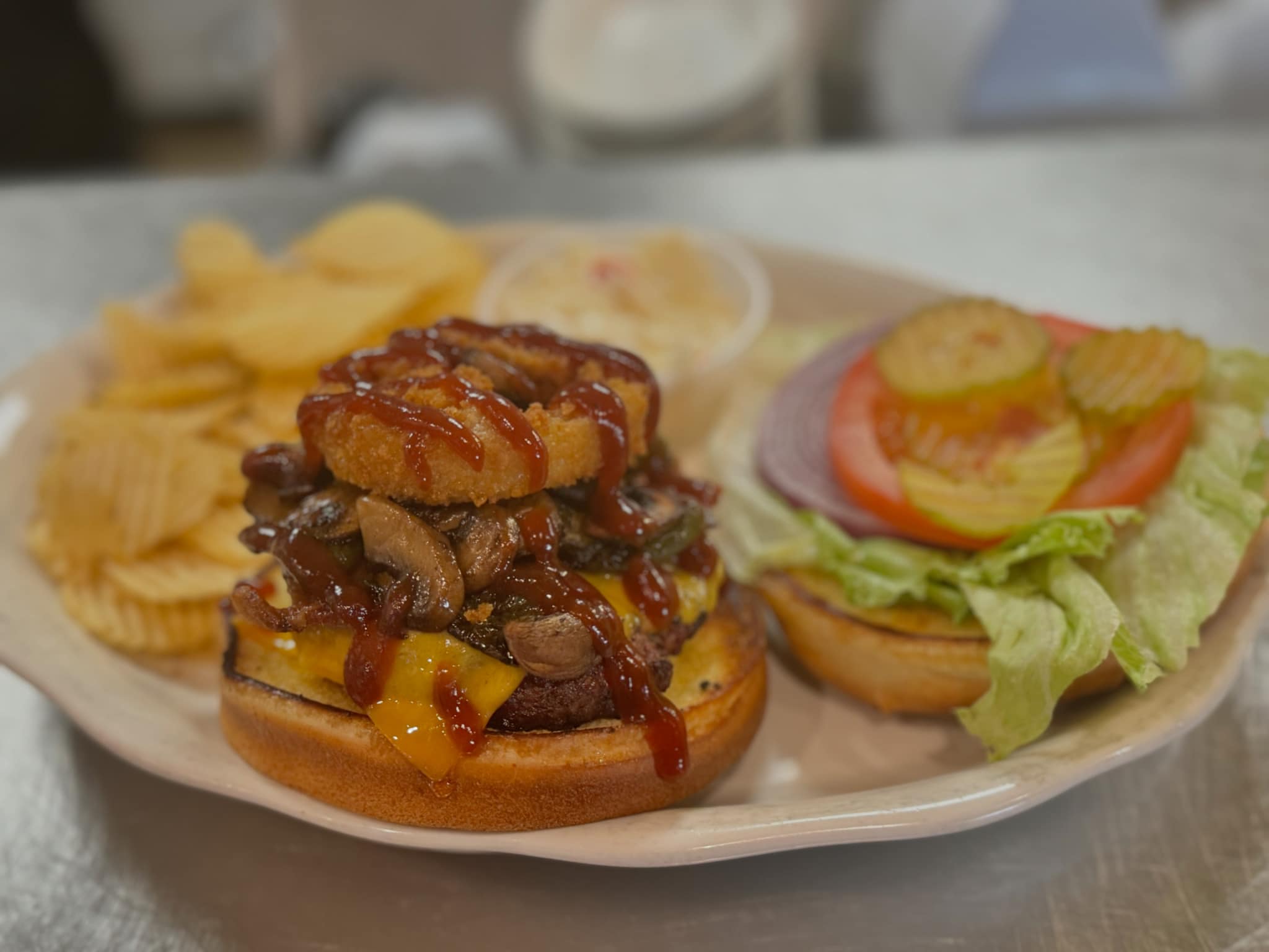 Loaded cheeseburger with mushrooms, onion ring, and BBQ sauce, served with ruffled potato chips.