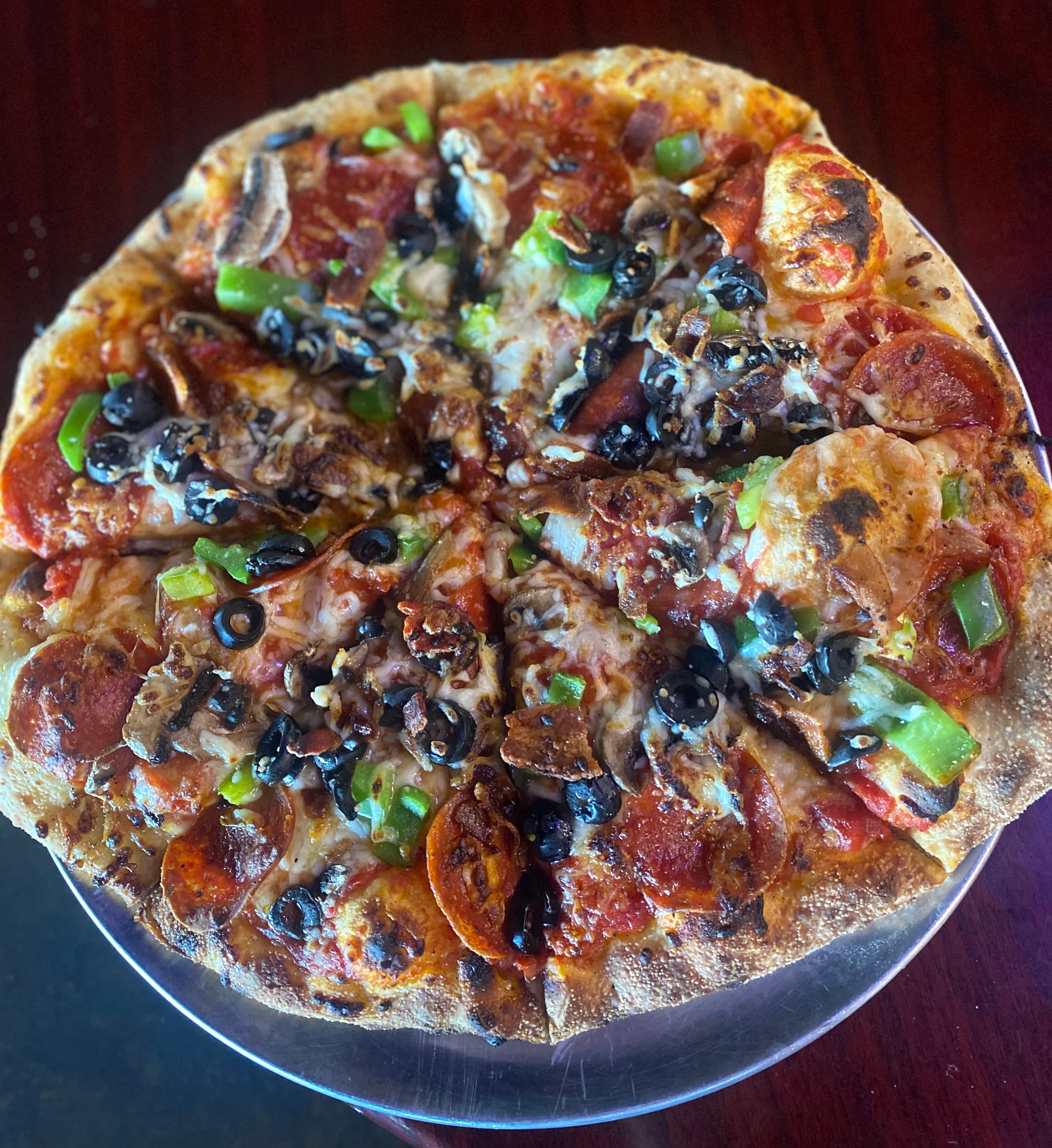 Supreme pizza with pepperoni, black olives, green peppers, and mushrooms on a metal tray.