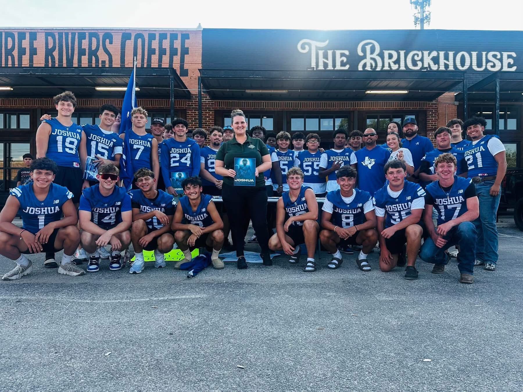 Joshua football players in blue jerseys pose with a woman in front of The Brickhouse.