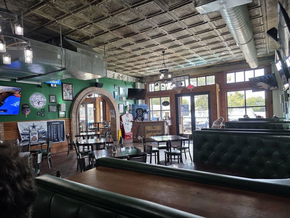 Sports bar interior with green booths, tin ceiling, brick archway, and sports memorabilia.